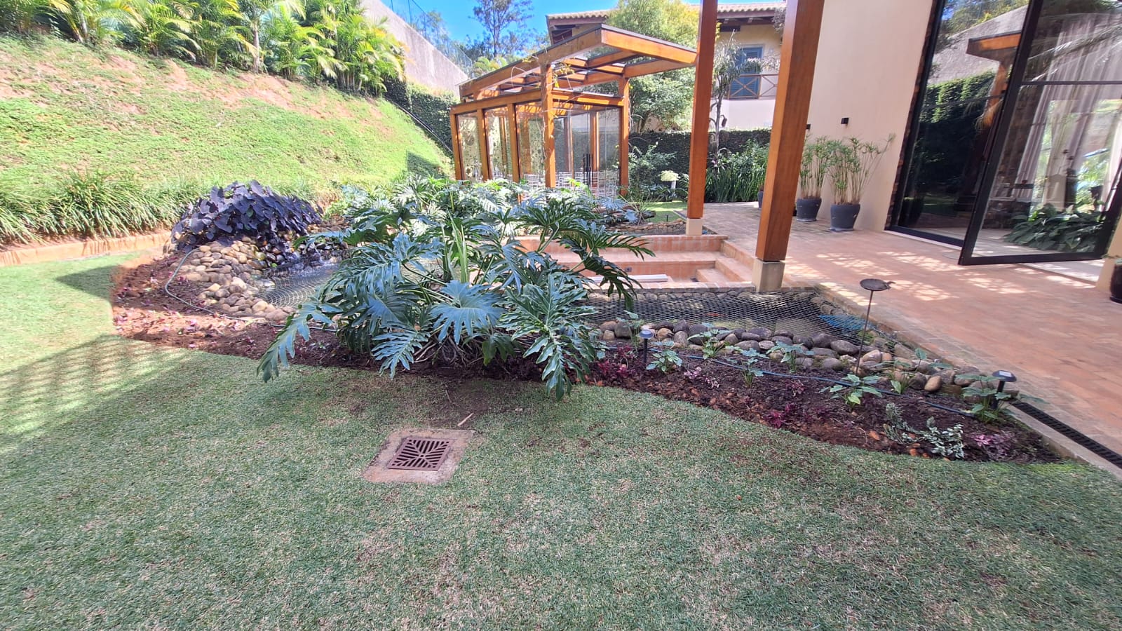 Jardim residencial com canteiro tropical, seixos e iluminação após o serviço